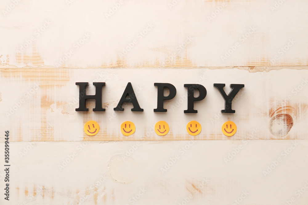 Word HAPPY and paper smiles on white wooden background