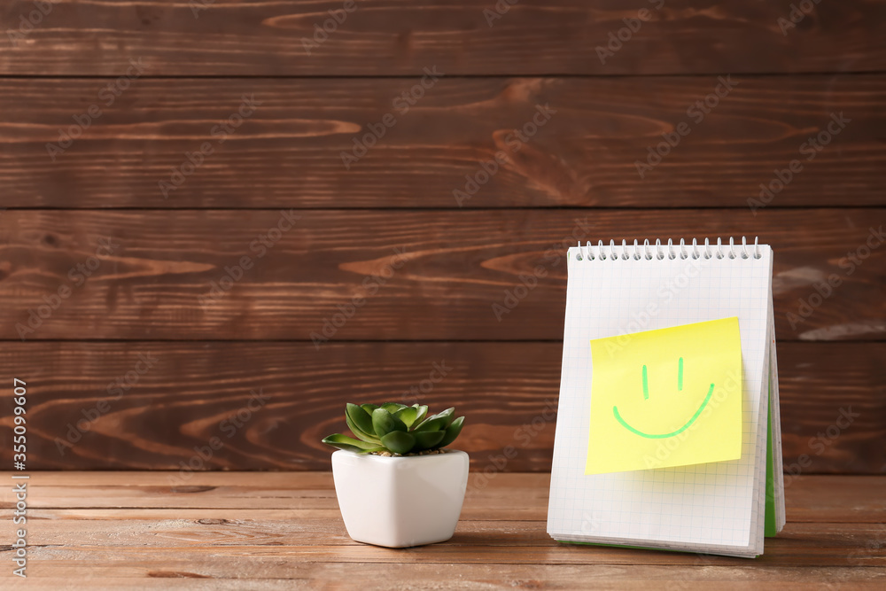 Notebook with drawn happy face on paper sheet against wooden background