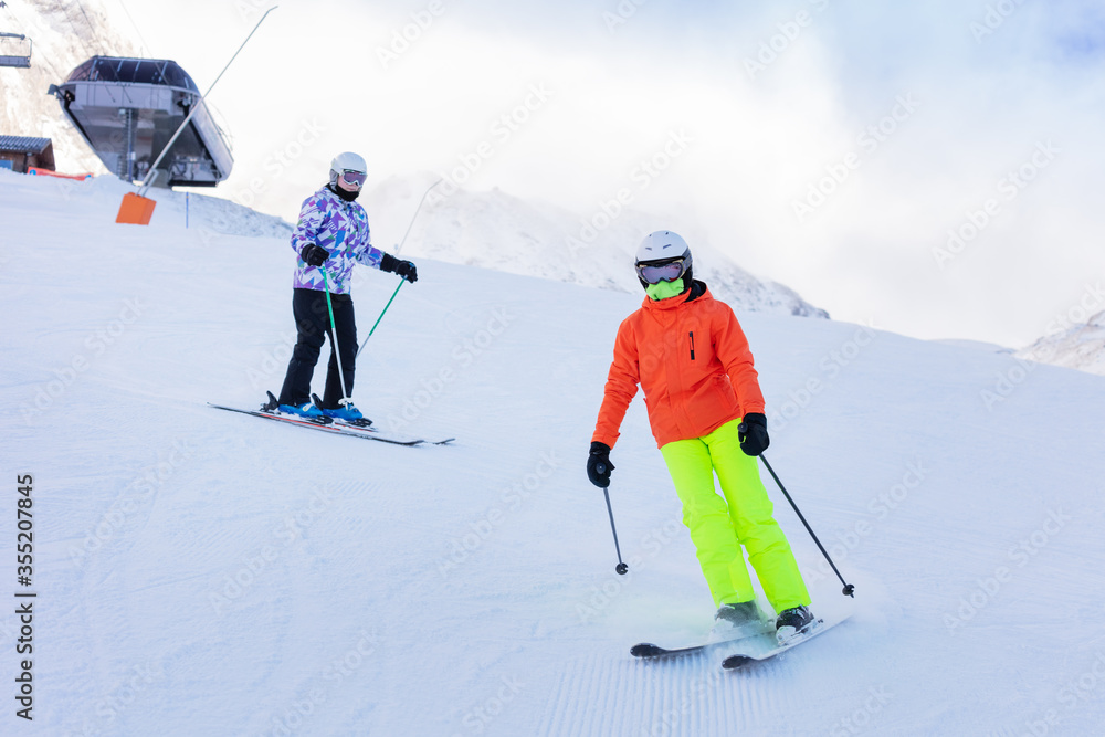 两个女孩穿着五颜六色的衣服在阿尔卑斯山的山坡上一起滑雪