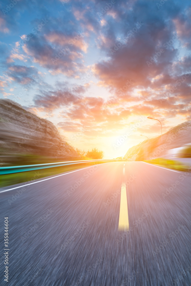 Motion blurred asphalt road and mountain landscape at sunset.