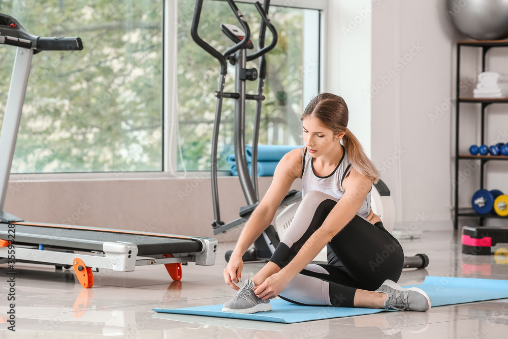 Sporty young woman tying shoelaces in gym