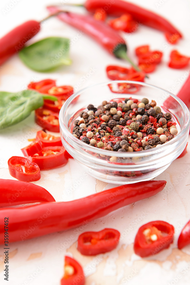 Hot chili pepper and bowl with peppercorn on light background