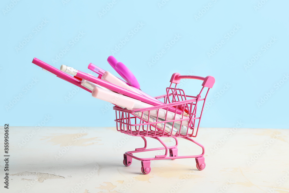 Set of stationery in shopping cart on color background