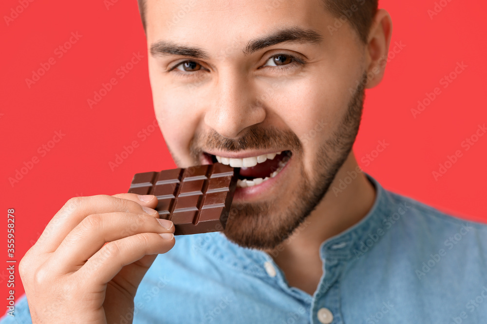 Handsome young man with tasty chocolate on color background