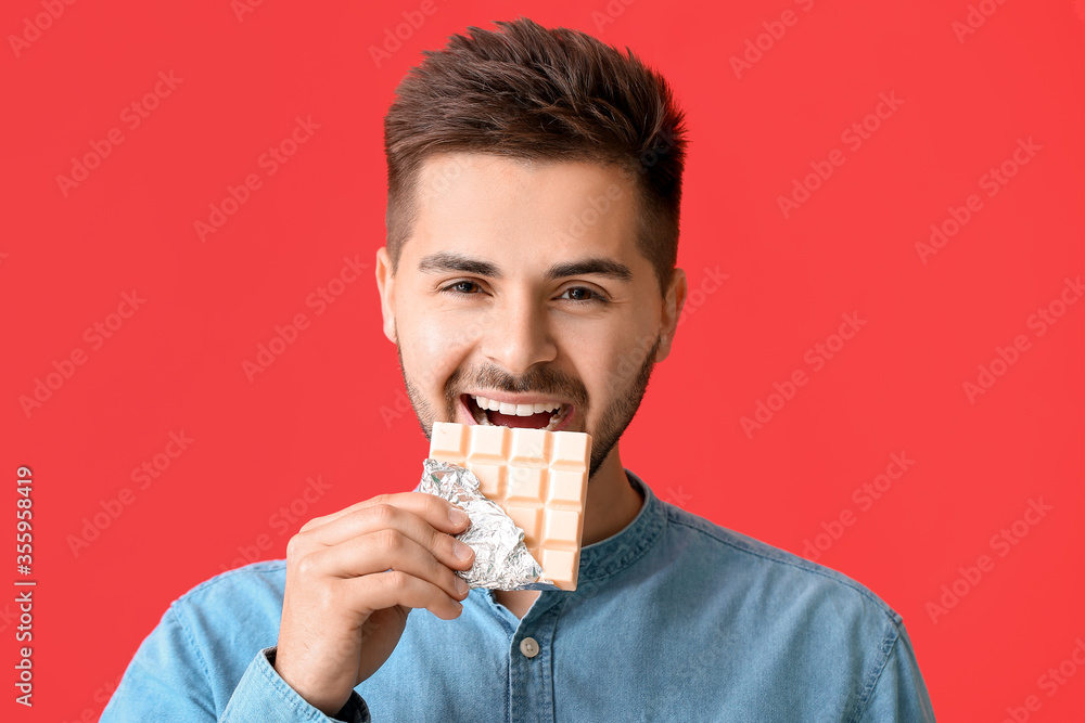 Handsome young man with tasty chocolate on color background