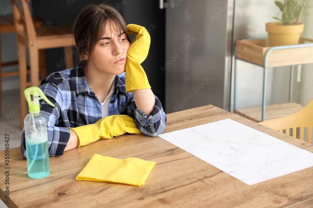 疲惫的年轻女子在厨房里拿着清洁用品