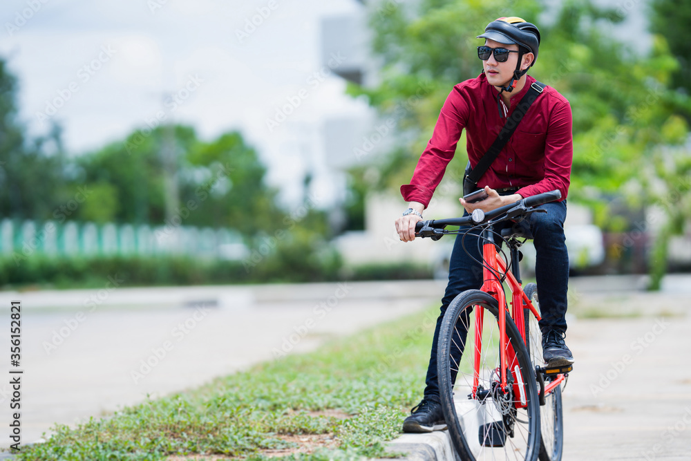 Asian man bicycles to work. He stops and uses his phone.