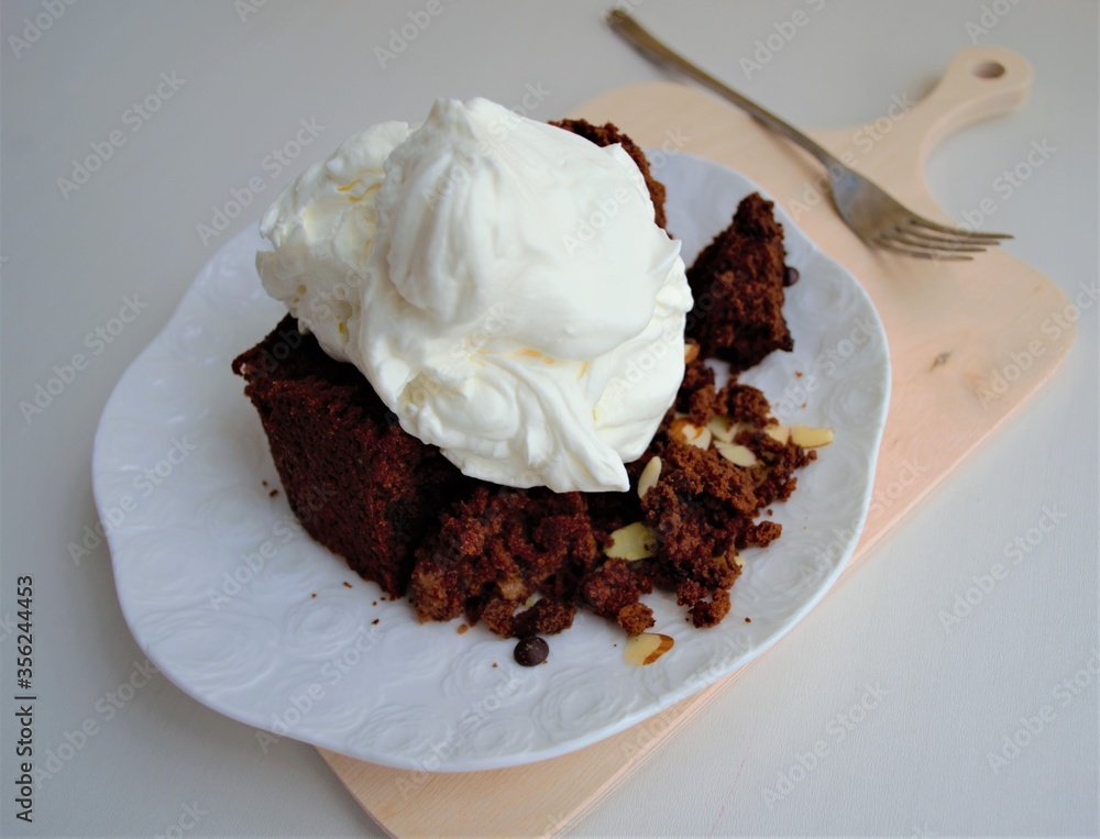 Homemade chocolate-nut dessert with whipped cream on top on a white glossy plate. Behind an iron for