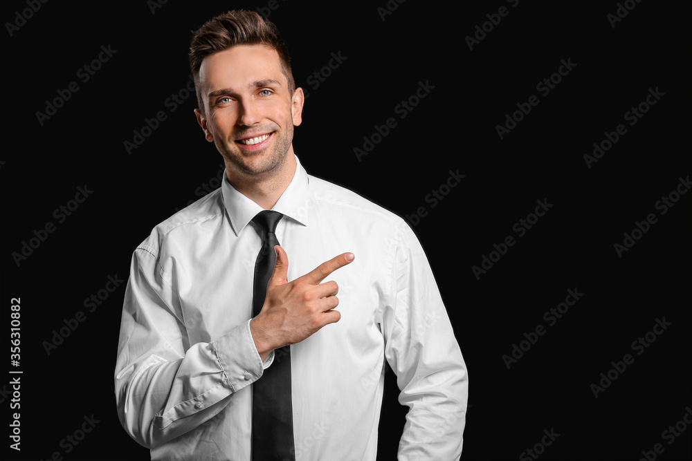 Portrait of handsome businessman showing something on dark background