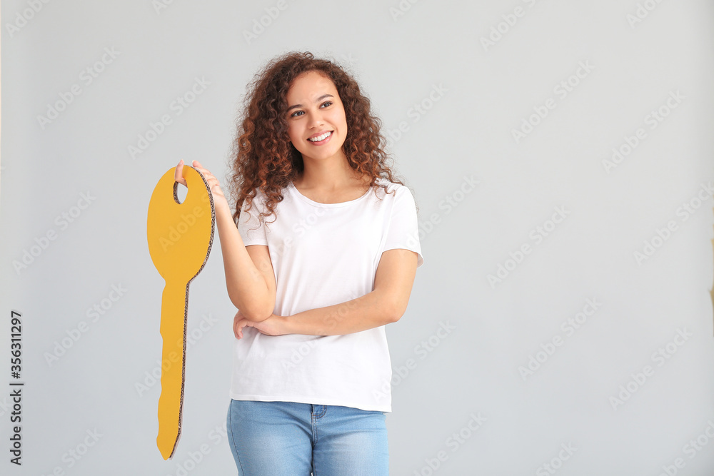 Young woman with big paper key on grey background