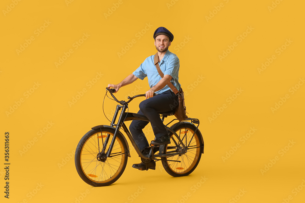 Handsome young postman with bicycle on color background