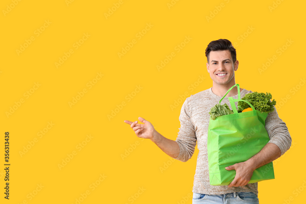 Young man with food in bag showing something on color background