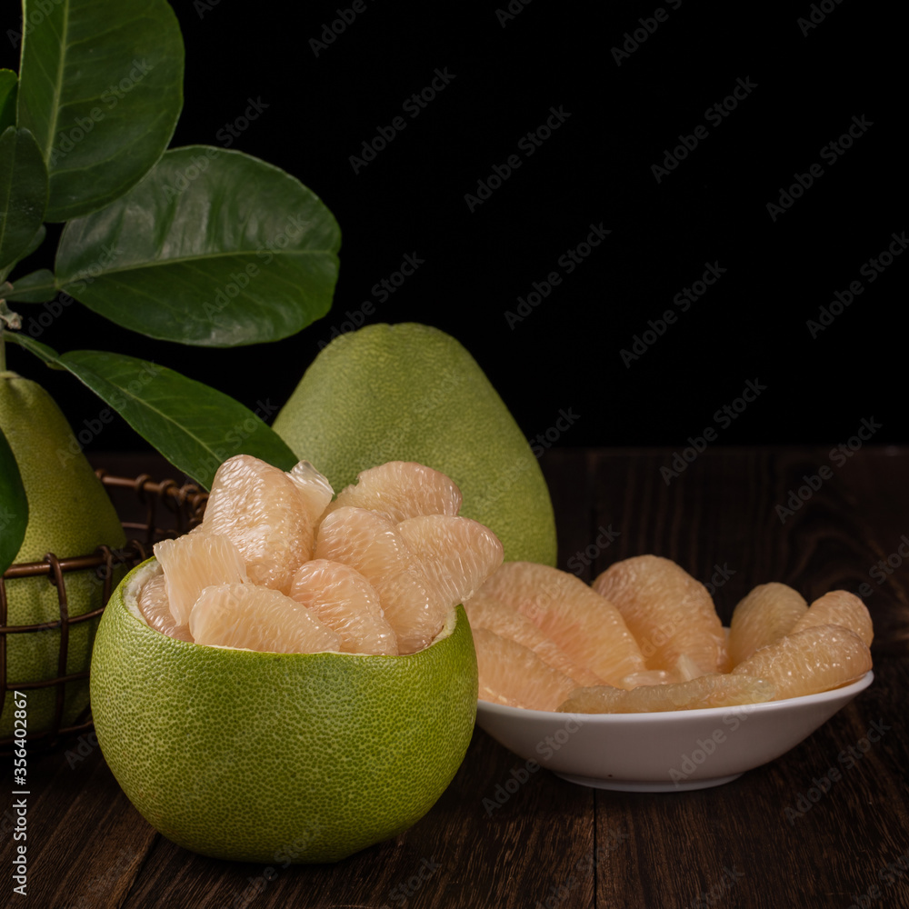 Fresh pomelo, pummelo, grapefruit, shaddock on wooden table over black background, close up, copy sp