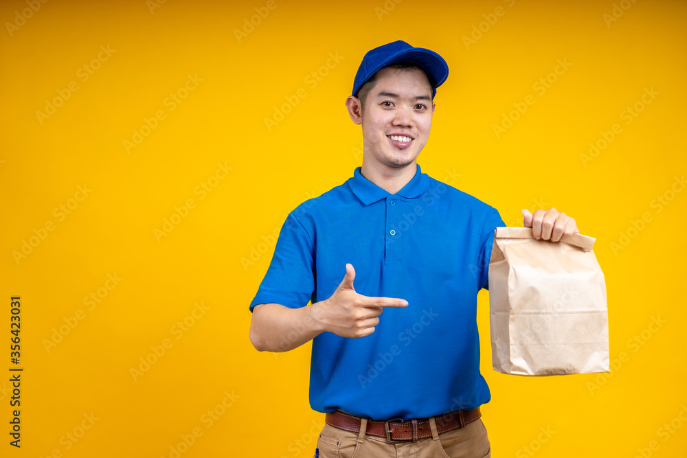 Asian delivery man holding fast food bag over yellow isolate background. Work from home and delivery