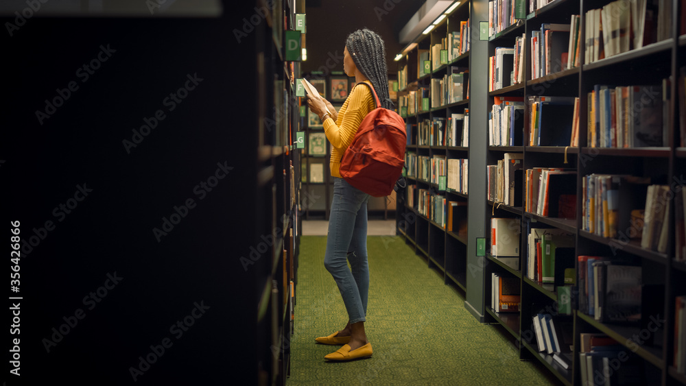 大学图书馆：天才美丽黑人女孩的肖像站在一排排书架之间