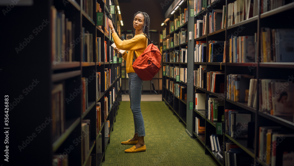 大学图书馆：天才美丽黑人女孩的肖像站在一排排书架之间