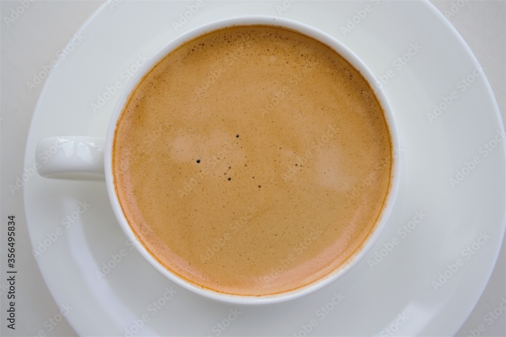 A white ceramic cup with a handle on a saucer and a coffee drink with a light brown pleasant foam. C