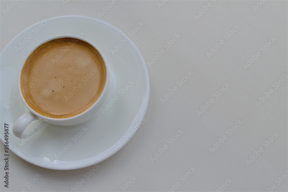 Composition of a white round cup with coffee standing on a saucer (left) and a light gray background