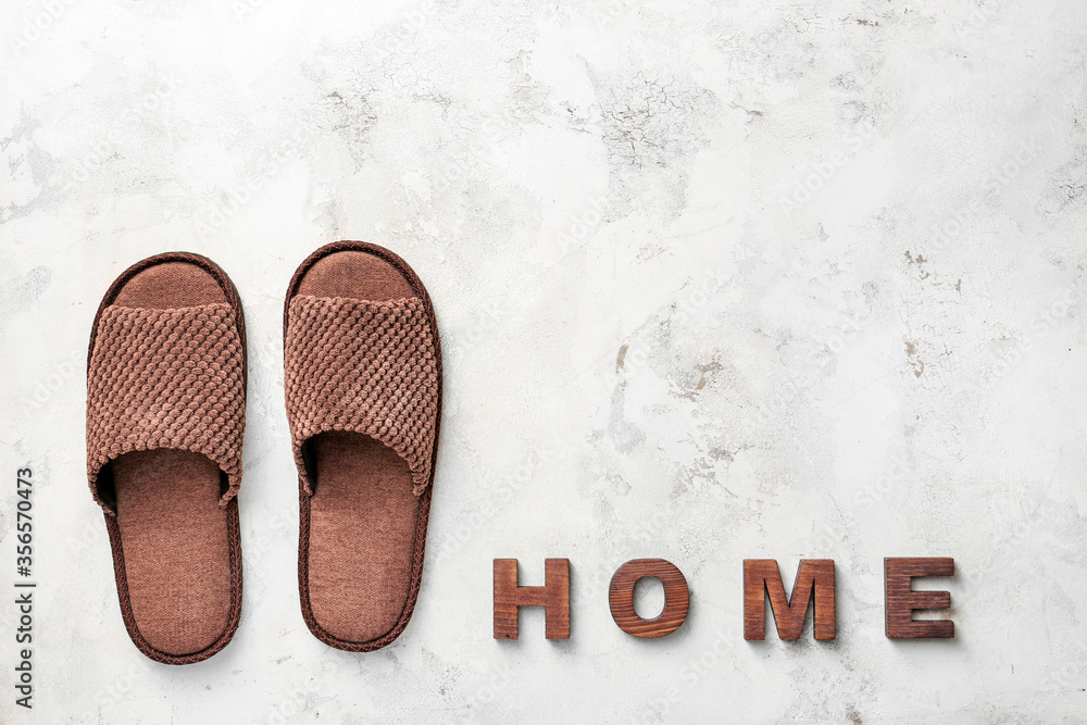 Pair of soft slippers and word HOME on light background