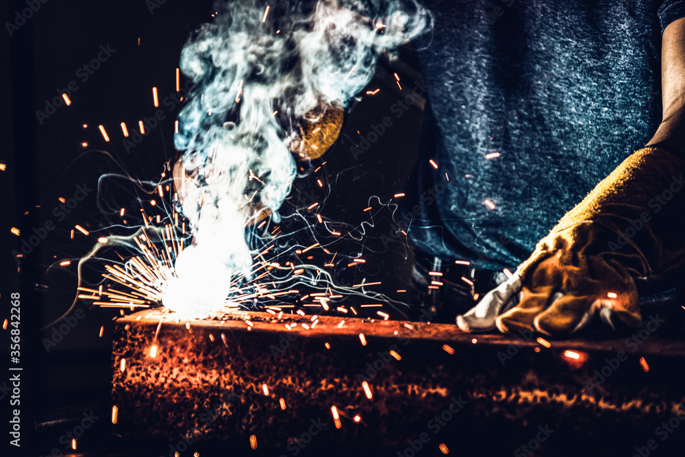 Metal welder working with arc welding machine to weld steel at factory while wearing safety equipmen