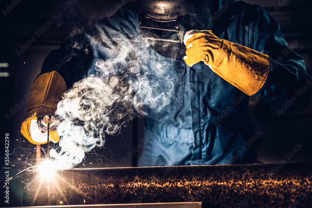 Metal welder working with arc welding machine to weld steel at factory while wearing safety equipmen