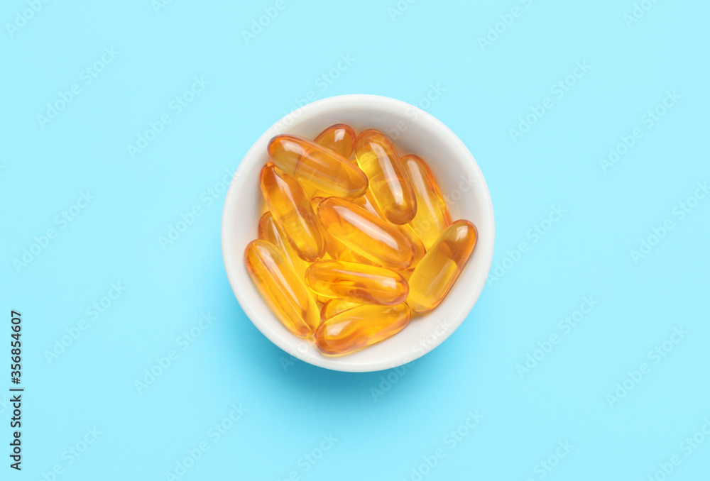 Bowl with fish oil capsules on color background