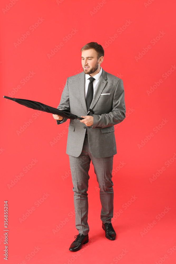 Handsome businessman with umbrella on color background