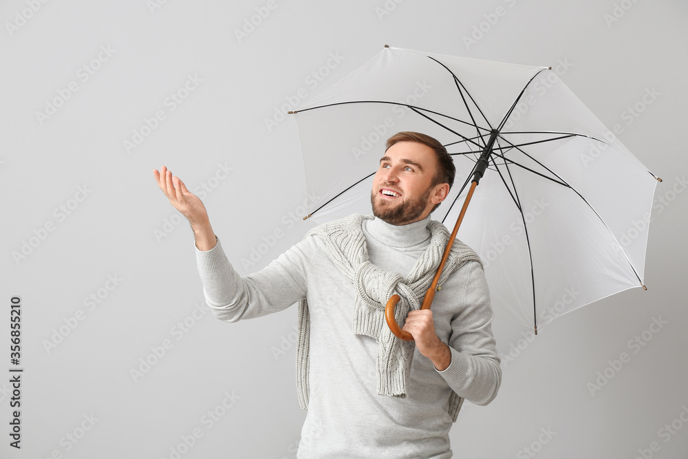 Handsome young man with umbrella on light background