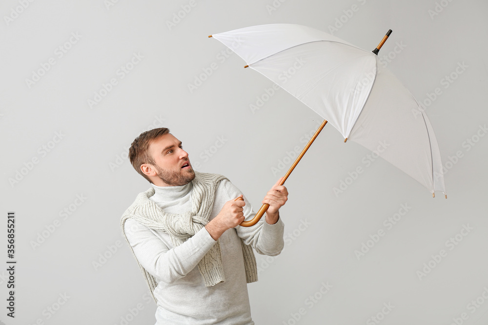 Handsome young man with umbrella on light background