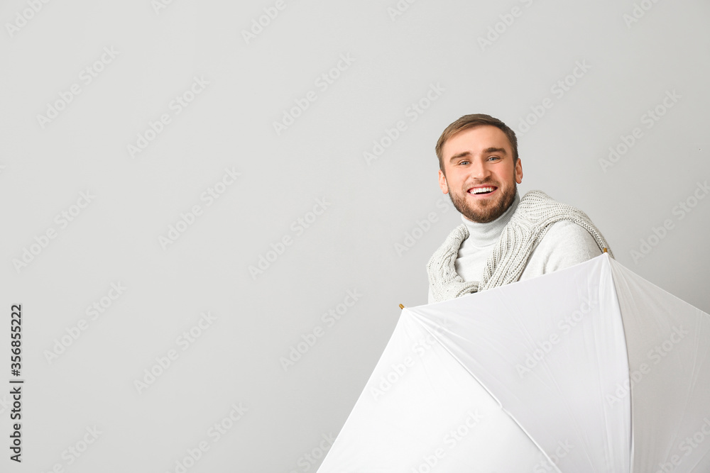 Handsome young man with umbrella on light background