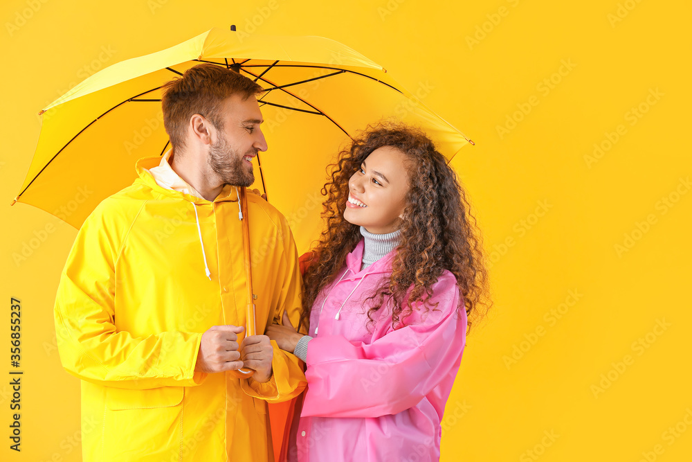 Happy young couple with umbrella on color background