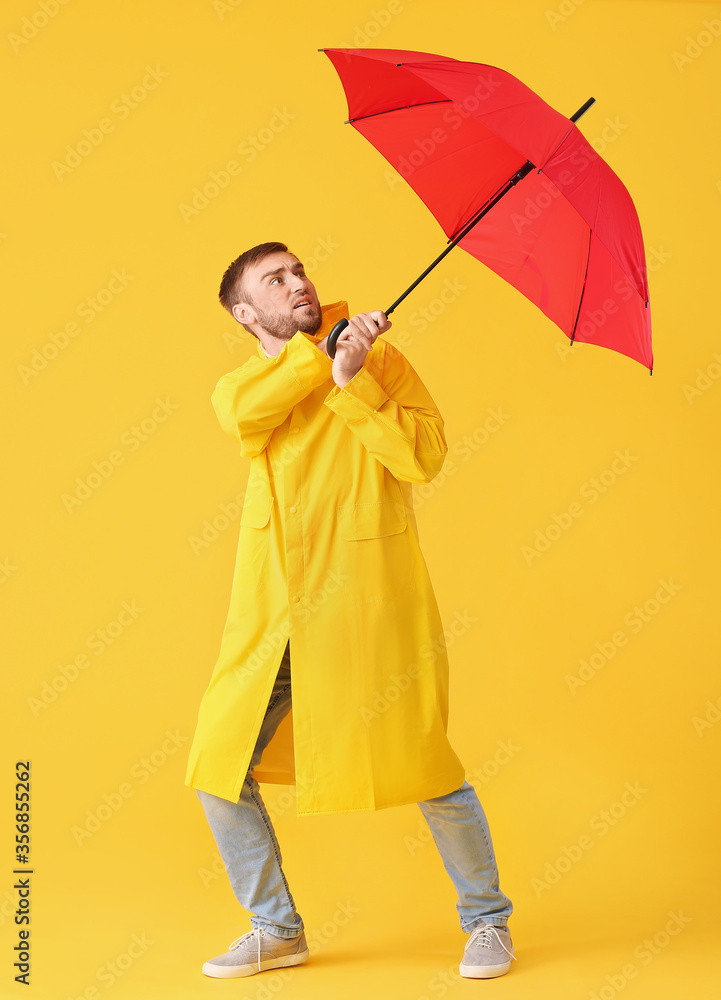 Handsome young man with umbrella on color background