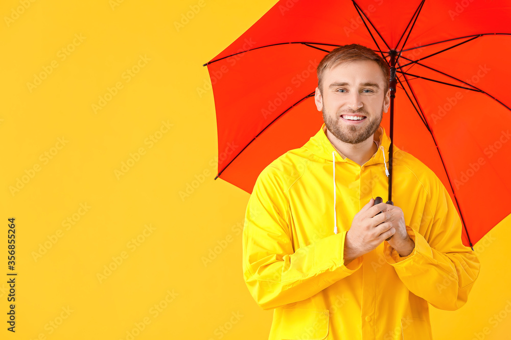 Handsome young man with umbrella on color background