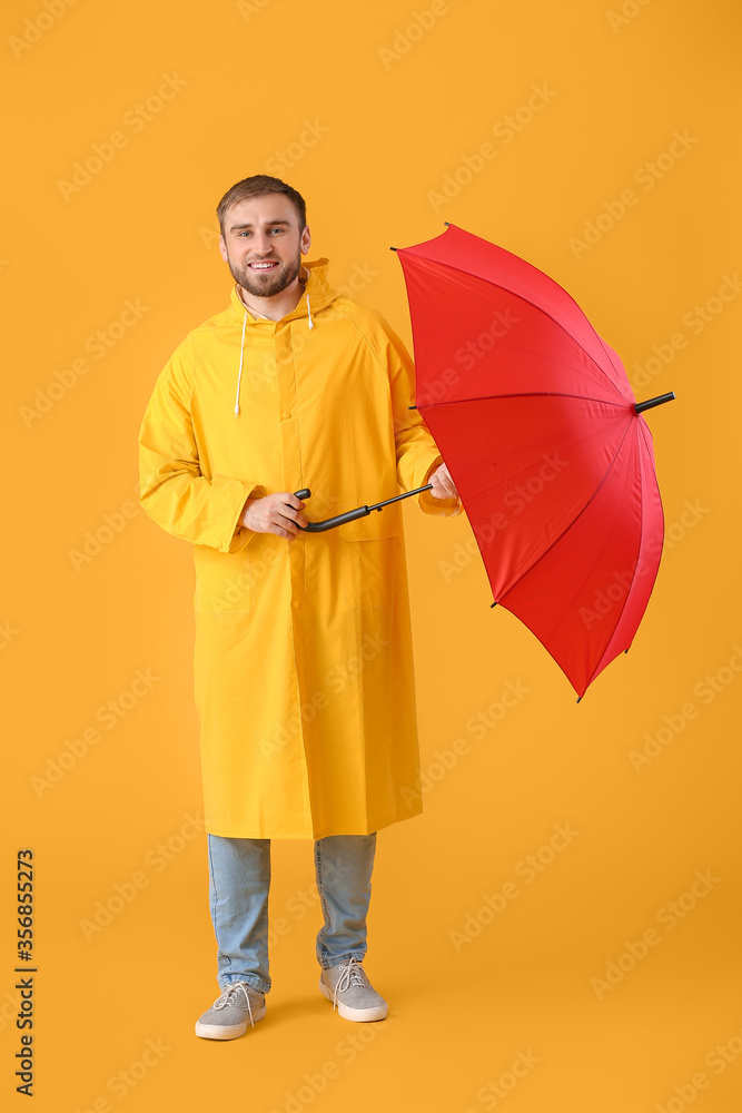 Handsome young man with umbrella on color background