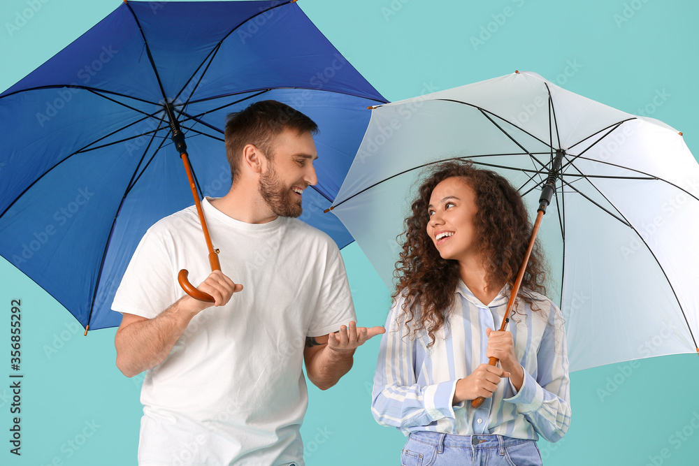 Happy young couple with umbrellas on color background