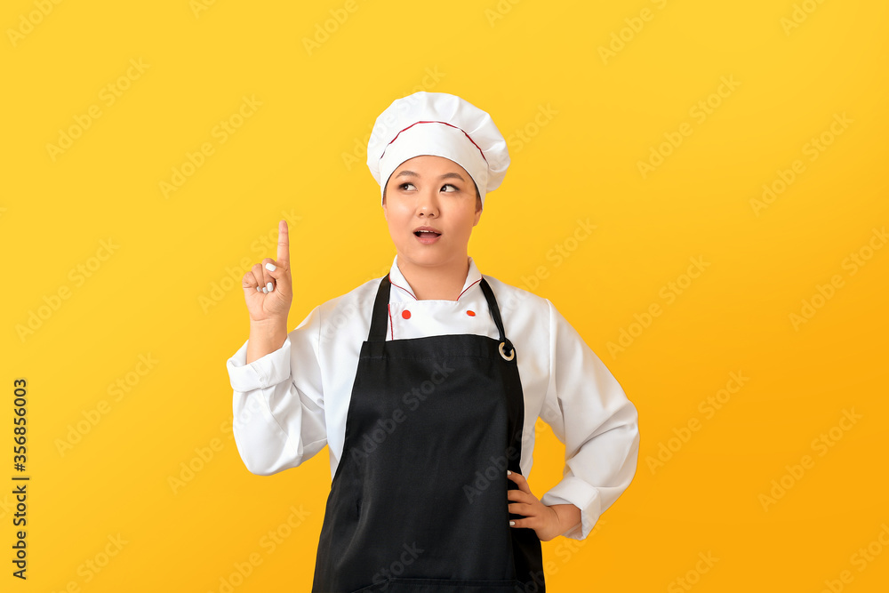 Beautiful Asian chef with raised index finger on color background