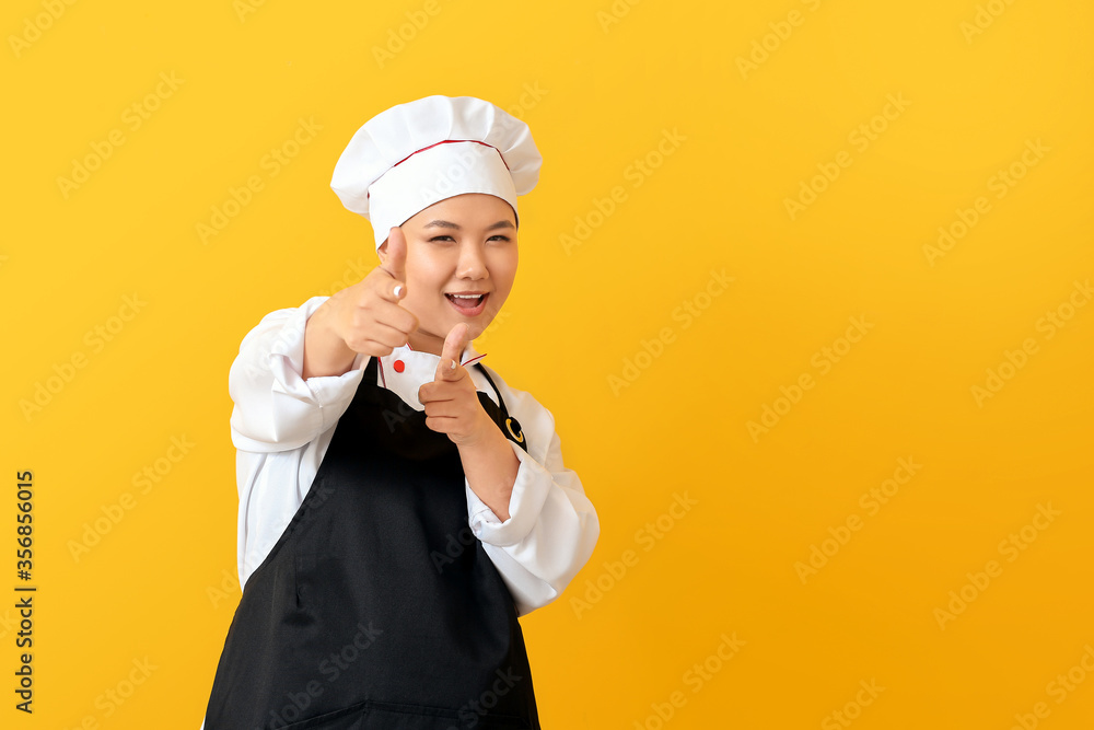 Beautiful Asian chef pointing at viewer on color background