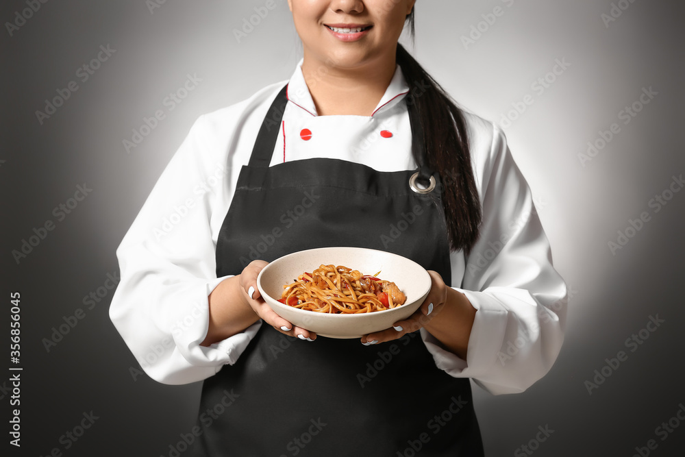 Beautiful Asian chef with dish on dark background