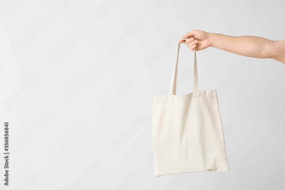 Male hand with eco bag on light background