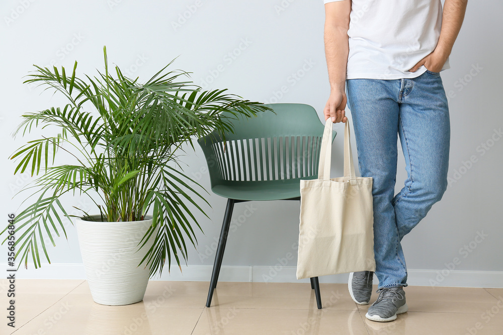 Young man with eco bag against light wall