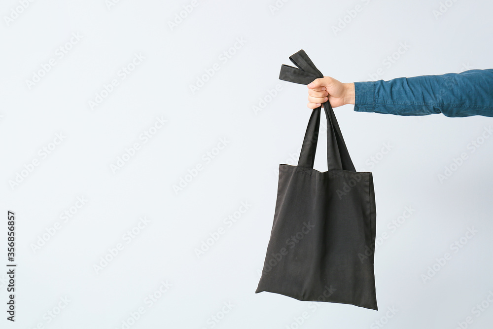 Male hand with eco bag on light background