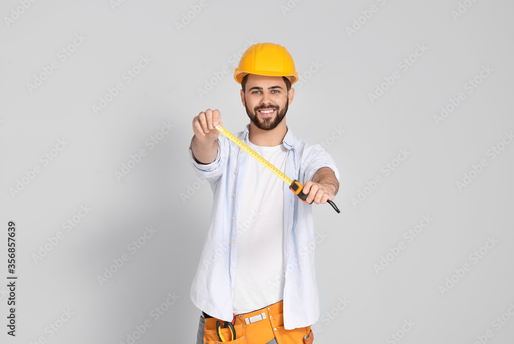 Young man with measuring tape on light background