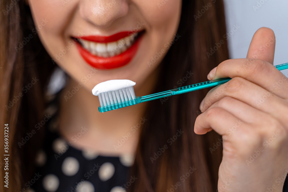 Woman with great teeth holding tooth brush in front of camera. Blurred background.