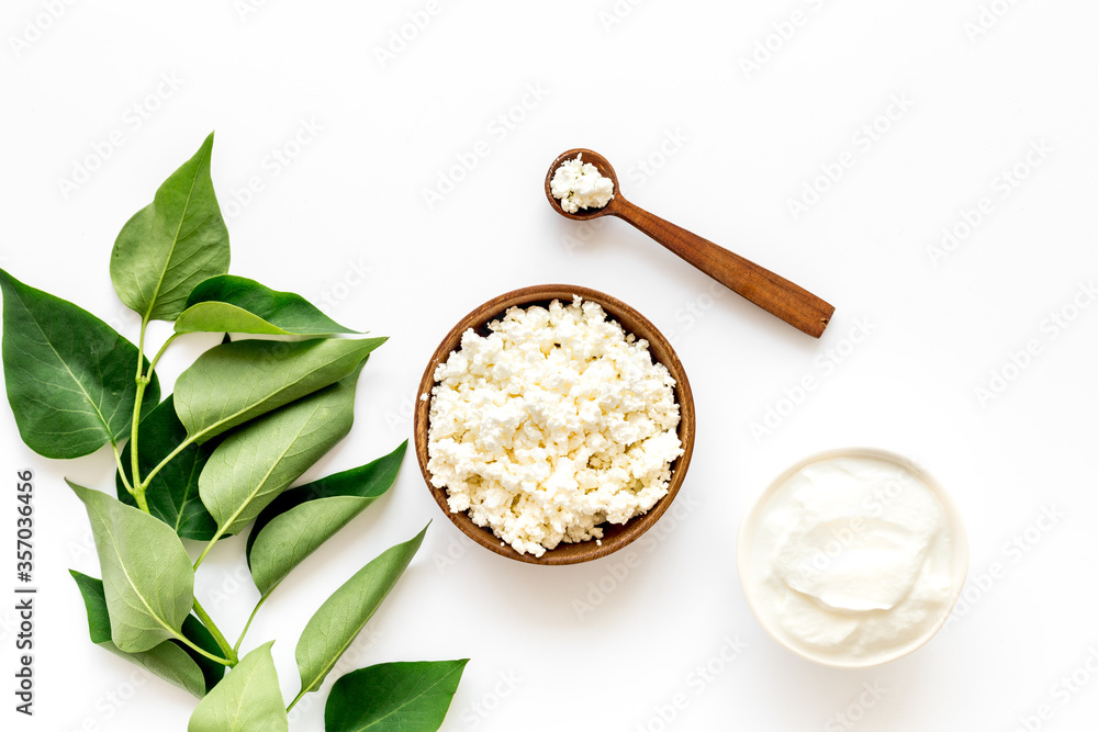 Cottage cheese in wooden bowl with green summer branch on white kitchen table. Top view 