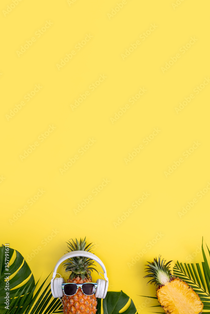 Funny pineapple wearing white headphone, listen music, isolated on yellow background with tropical p