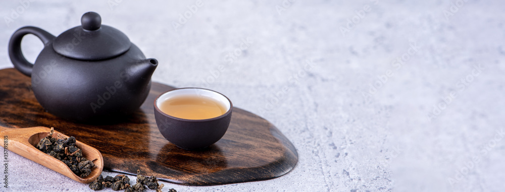 Hot tea in black teapot and cups and dry tea leaves over bright gray cement background, close up, co