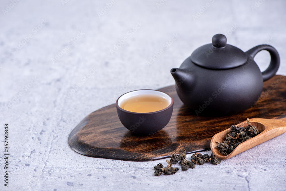 Hot tea in black teapot and cups and dry tea leaves over bright gray cement background, close up, co