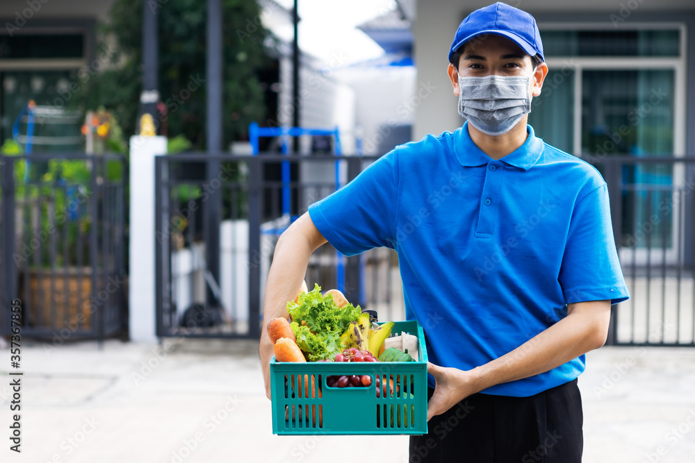 亚洲送货员身穿蓝色制服，戴医用口罩，为杂货店提供新鲜食品t