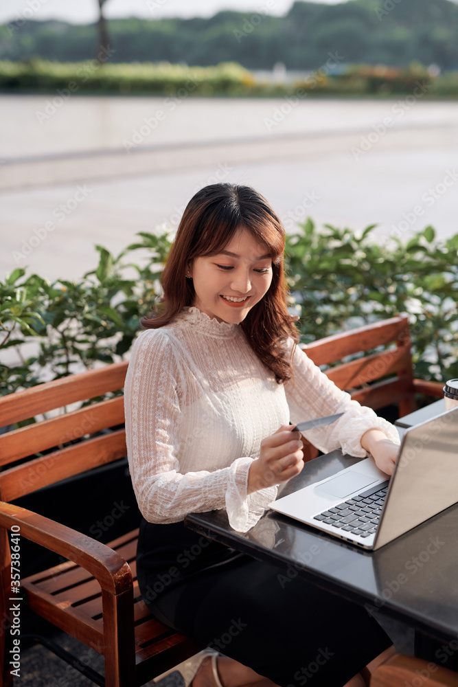 休闲女孩用笔记本电脑在网上购物，在街上的咖啡店用信用卡付款