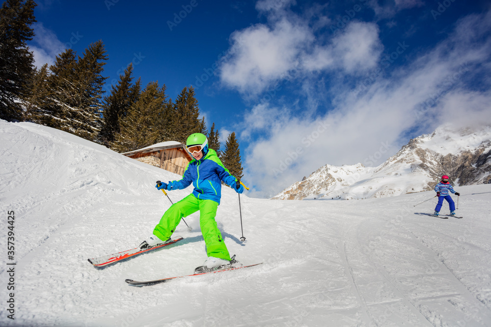 Two kids 10 years old racing down the slope on sunny day in Alpes mountains in colorful outfit